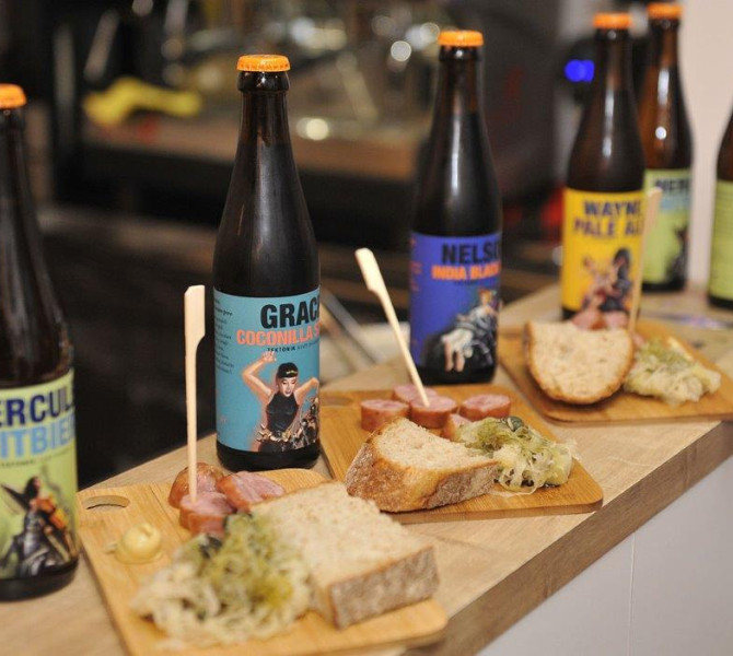 Pet različnih vrst piva na lesenem šanku. Ob pivu na deski narezan kruh, klobasa in namaz.