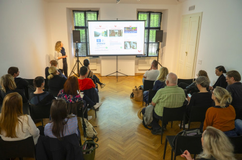 Predavateljica in slusatelji v prostoru gledaja vpresentacijo.