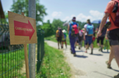 Skupina ljudi hodi po poti. Oznaka poti s puscico in napisom 'Cankjarjeva pot'.