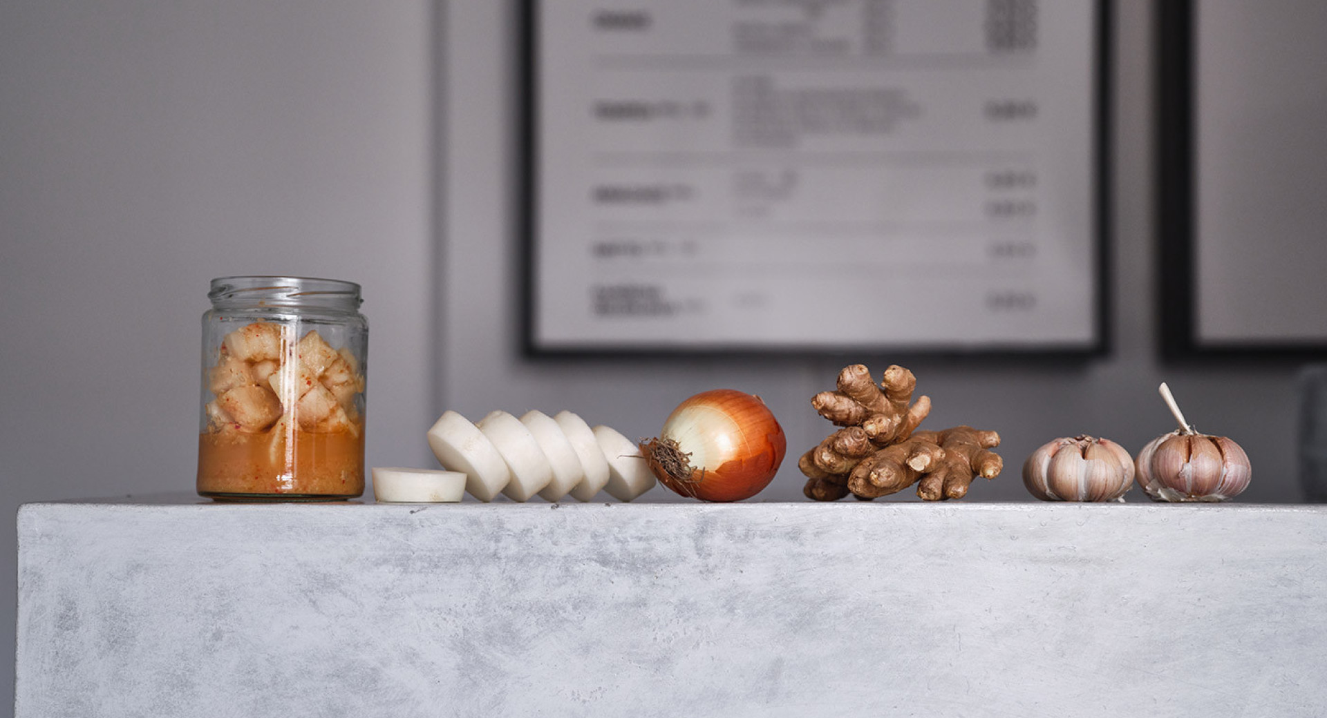 Zbir pridelkov na marmornati mizi: z leve proti desni omaka v kozarcu, narezan por, čebula, ingver in česen