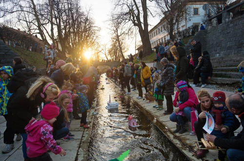 Odrasli in otroci spuscajo papirnate barcice po reki.