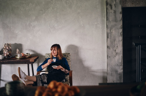 Ženska sedi, v rokah drži skodelico in krožnik zanjo.