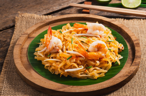 A wooden plate with noodles, sprouts, and shrimp.