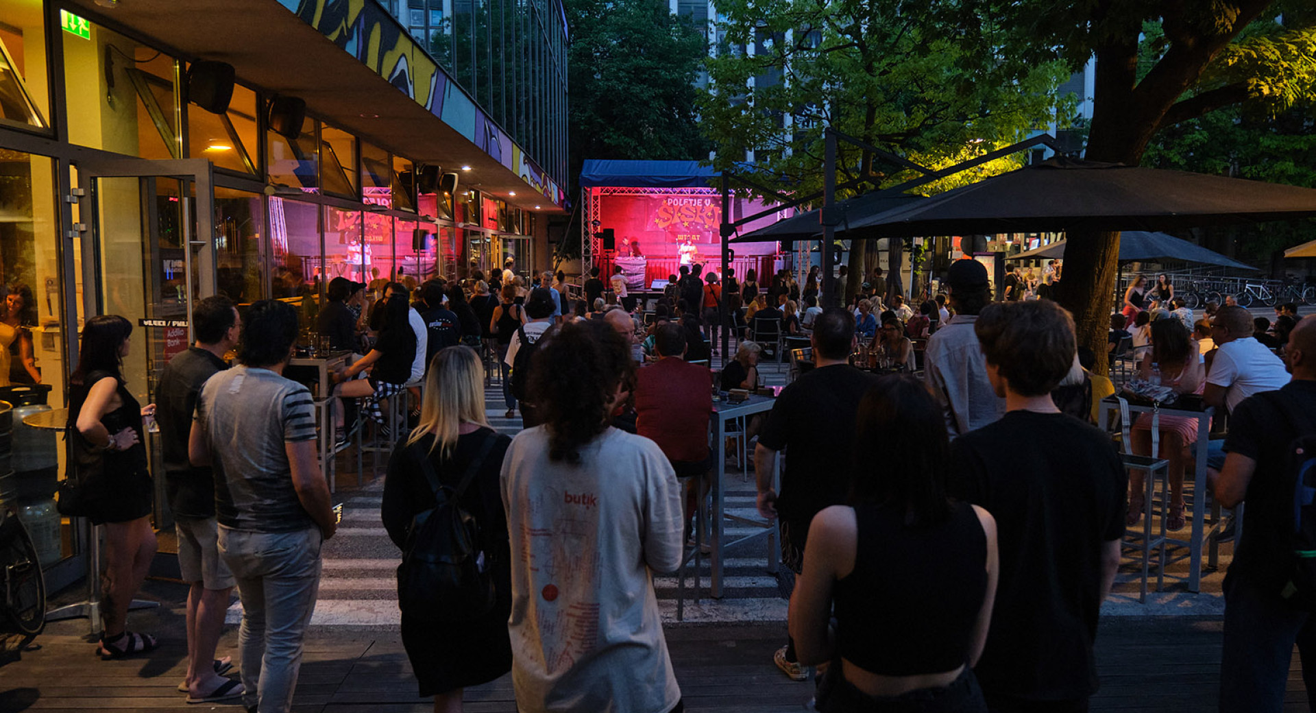 People sit at café tables, chatting and listening to a musical performance.