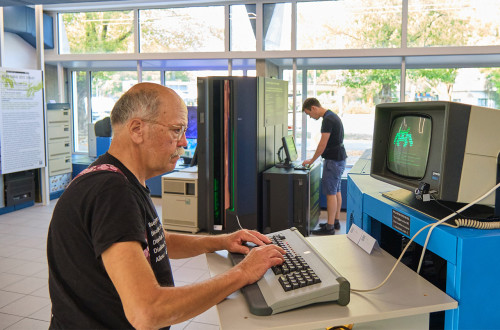 An older man types on a computer. A vintage computer is displaying a game