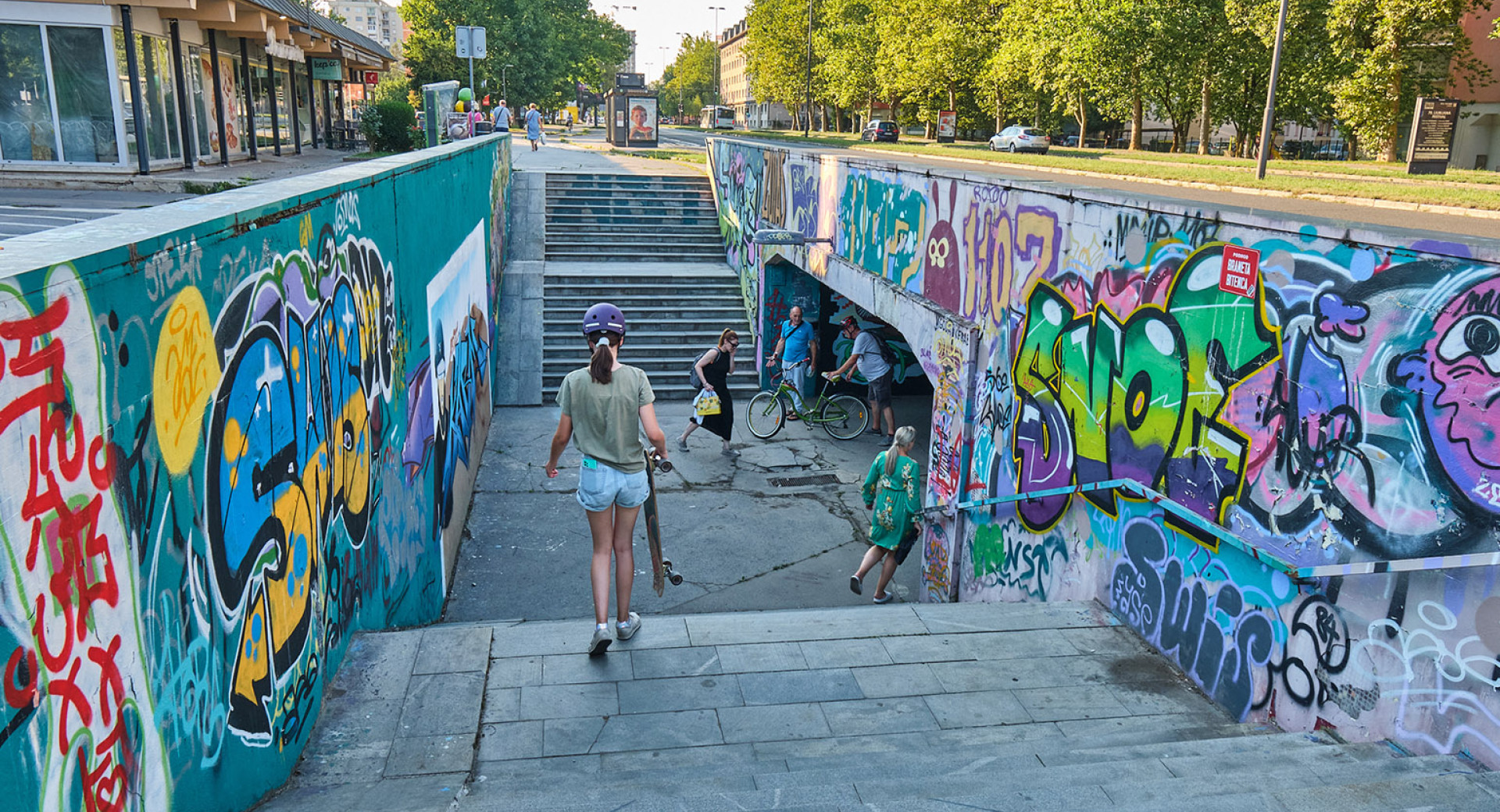 A graffiti-covered underpass in an urban environment. People are walking through the underpass.