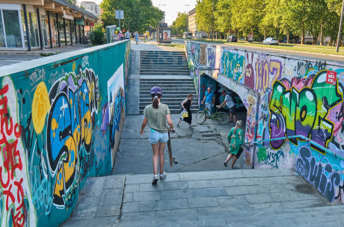 A graffiti-covered underpass in an urban environment. People are walking through the underpass.