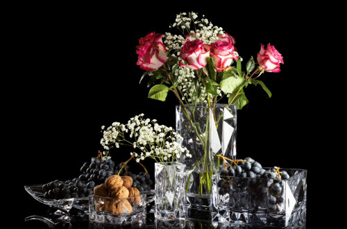 Pink roses arranged with white flowers, grapes, and walnuts in decorative crystal bowls.