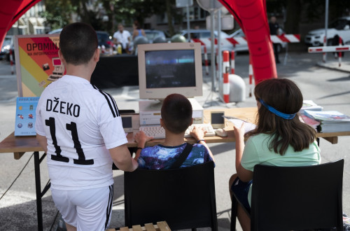 Three children are watching a computer while one child is playing a game.