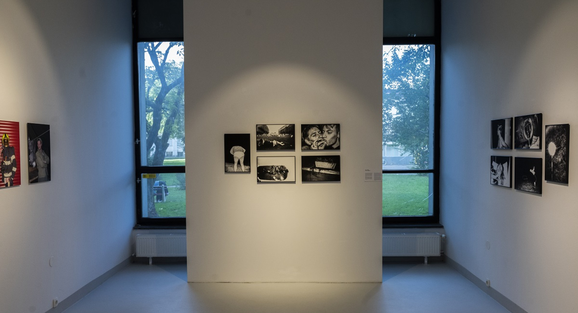 Black and white photographs on display. A room with white walls and two windows.