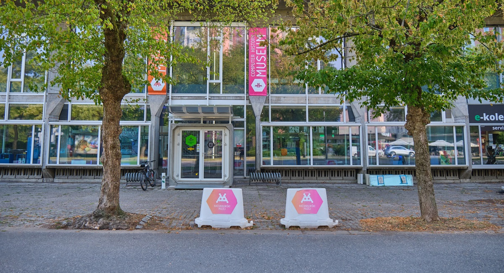 The kiosk is in front of a glass building, with two trees nearby.