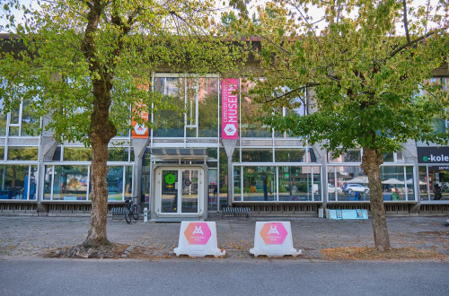 The kiosk is in front of a glass building, with two trees nearby.