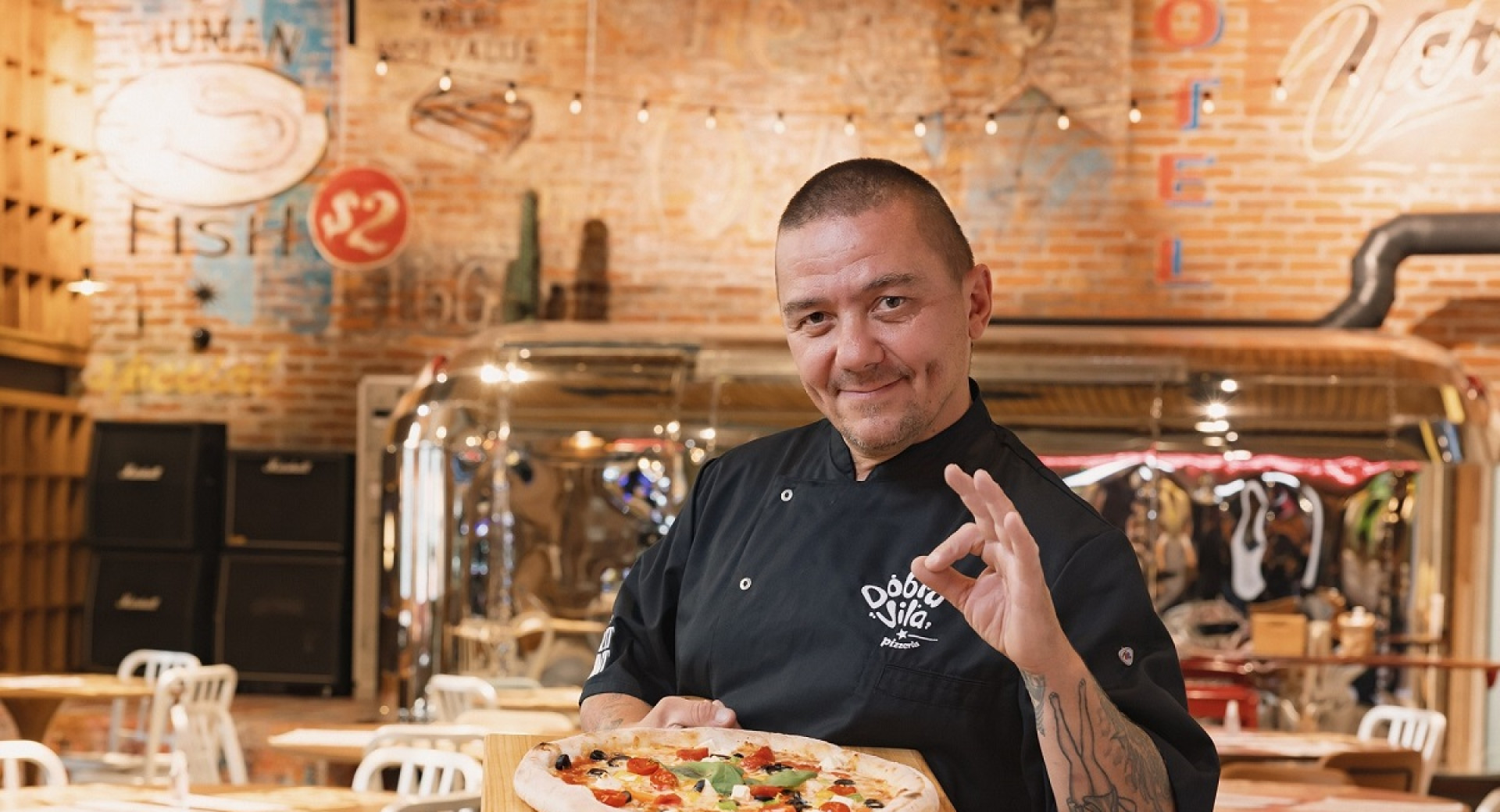 Chef in black with pizza on a tray.