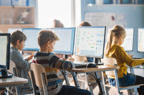 Children sit at computers. The children are learning to program.