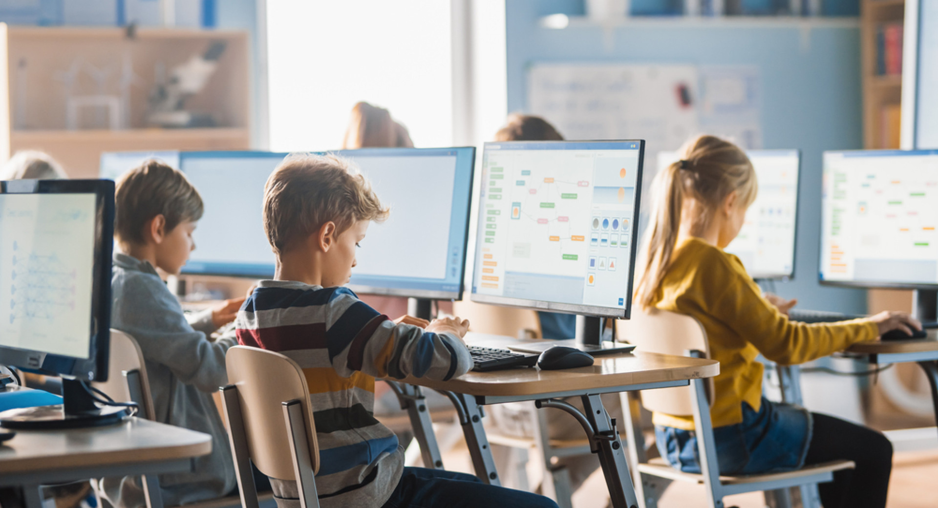 Children sit at computers. The children are learning to program.