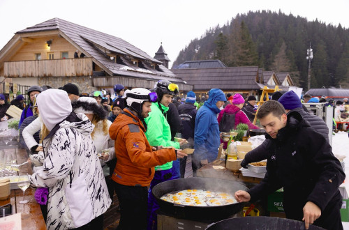 Ljudje v smučarskih oblačilih na kulinarični prireditvi na smučišču.