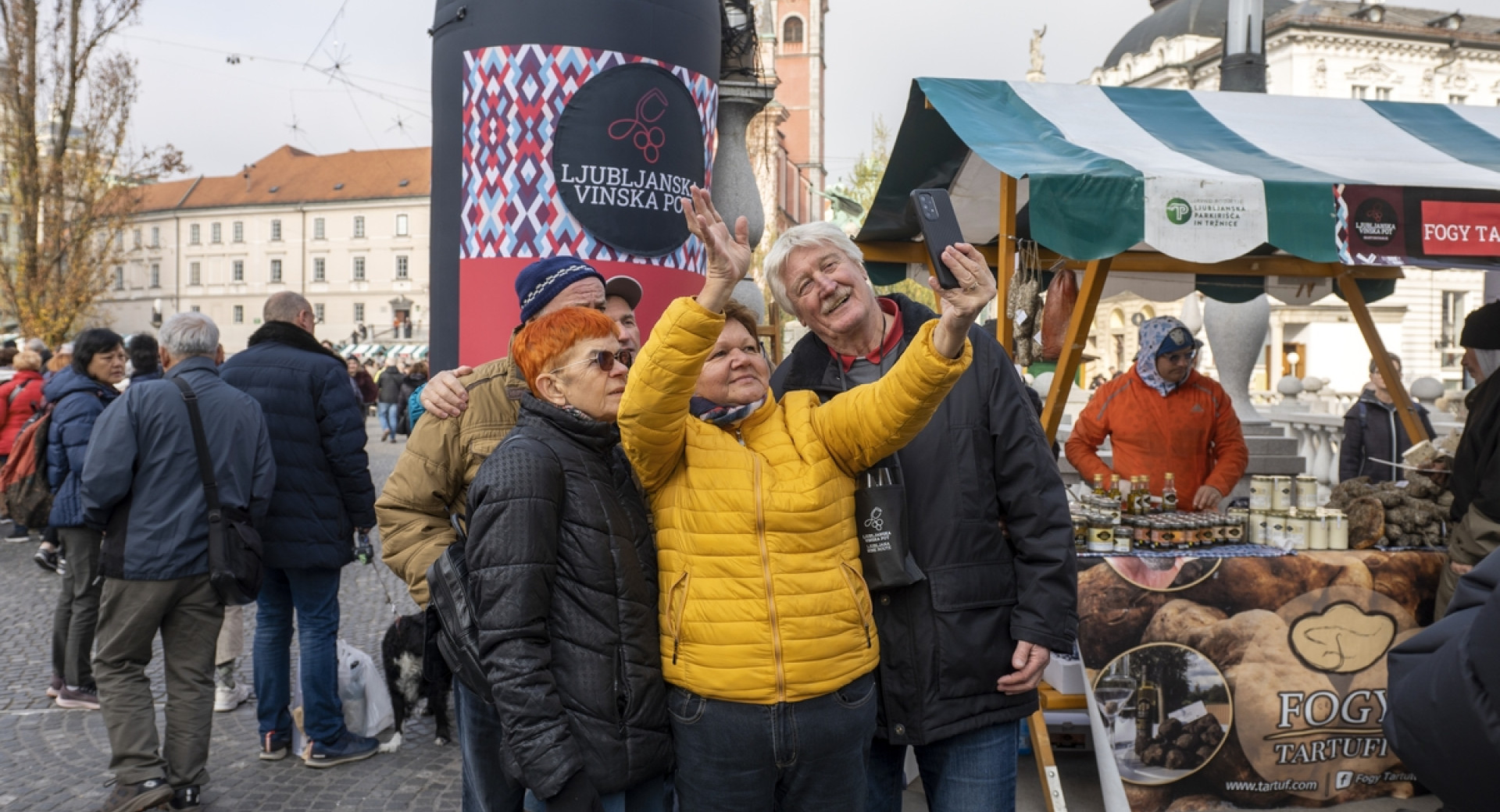 Manjša skupina ljudi med snemanjem sebka pred veliko steklenico vina.