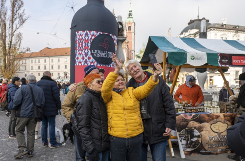 Manjša skupina ljudi med snemanjem sebka pred veliko steklenico vina.