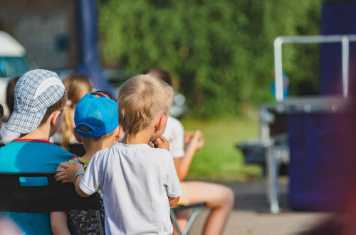 Children are sitting outside, watching a performance.