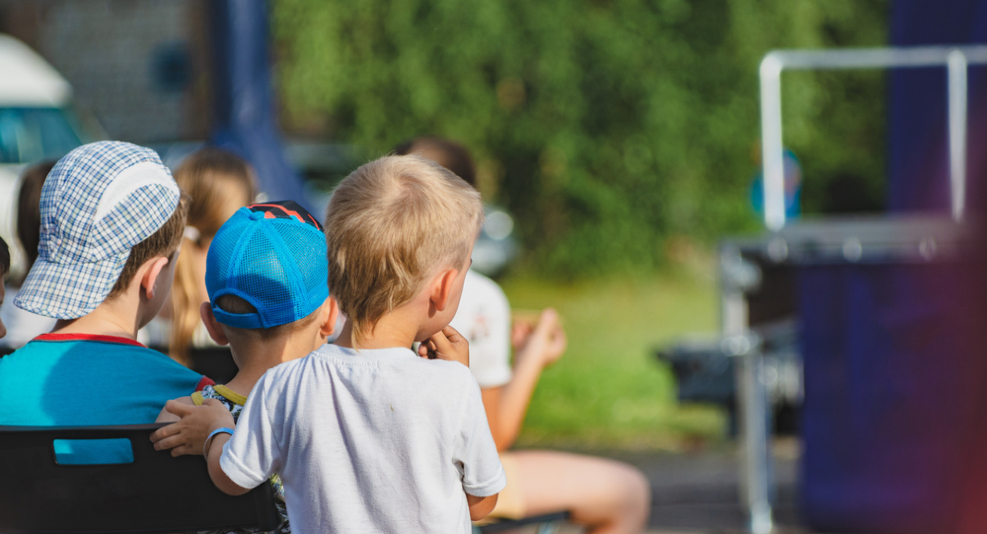 Children are sitting outside, watching a performance.