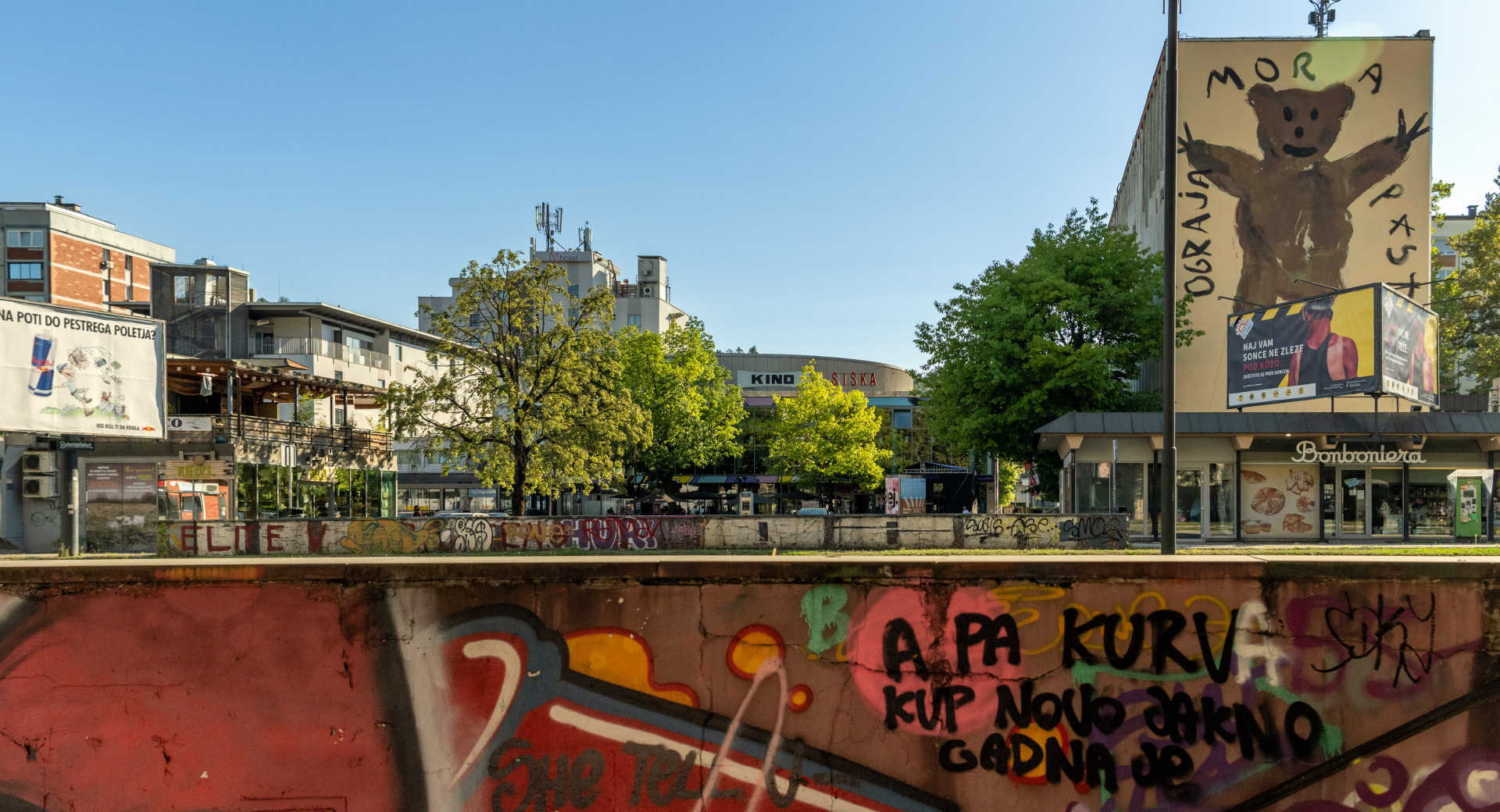 grafiti na zidu, v ozadju stavba s poslikavo medveda, drevesa