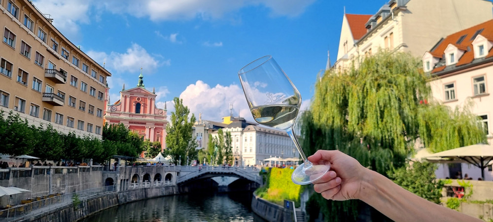 A person holding a glass of white wine with a view of Ljubljana's historic city center