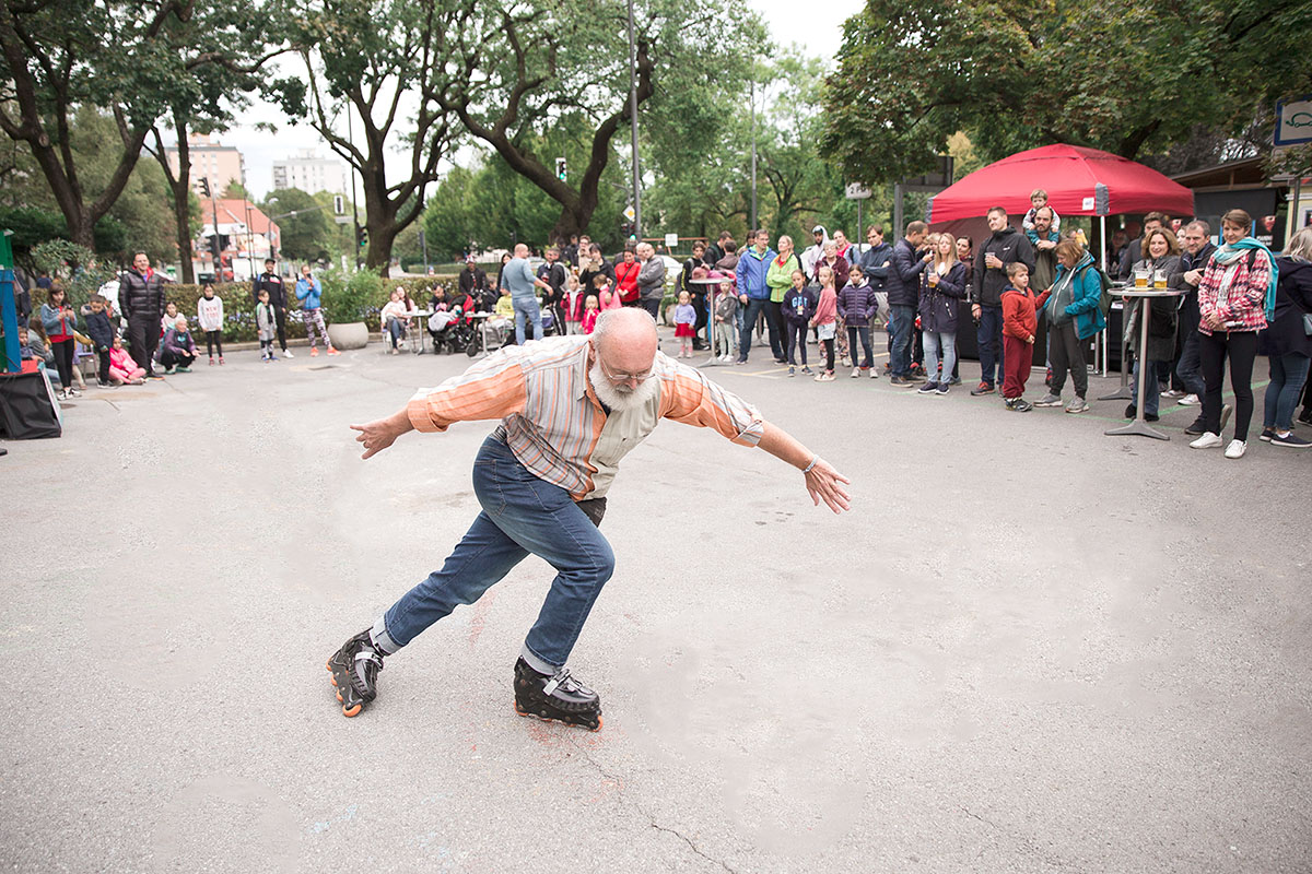 An older man on rollerblades is performing tricks in the middle of a crowd of onlookers.