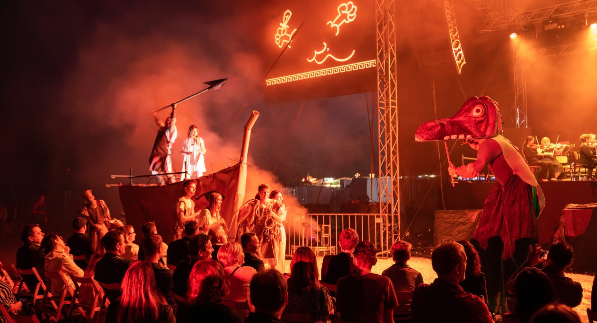 People at a concert in front of a huge wooden boat with a man in white.