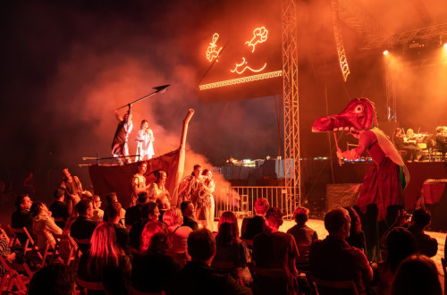 People at a concert in front of a huge wooden boat with a man in white.