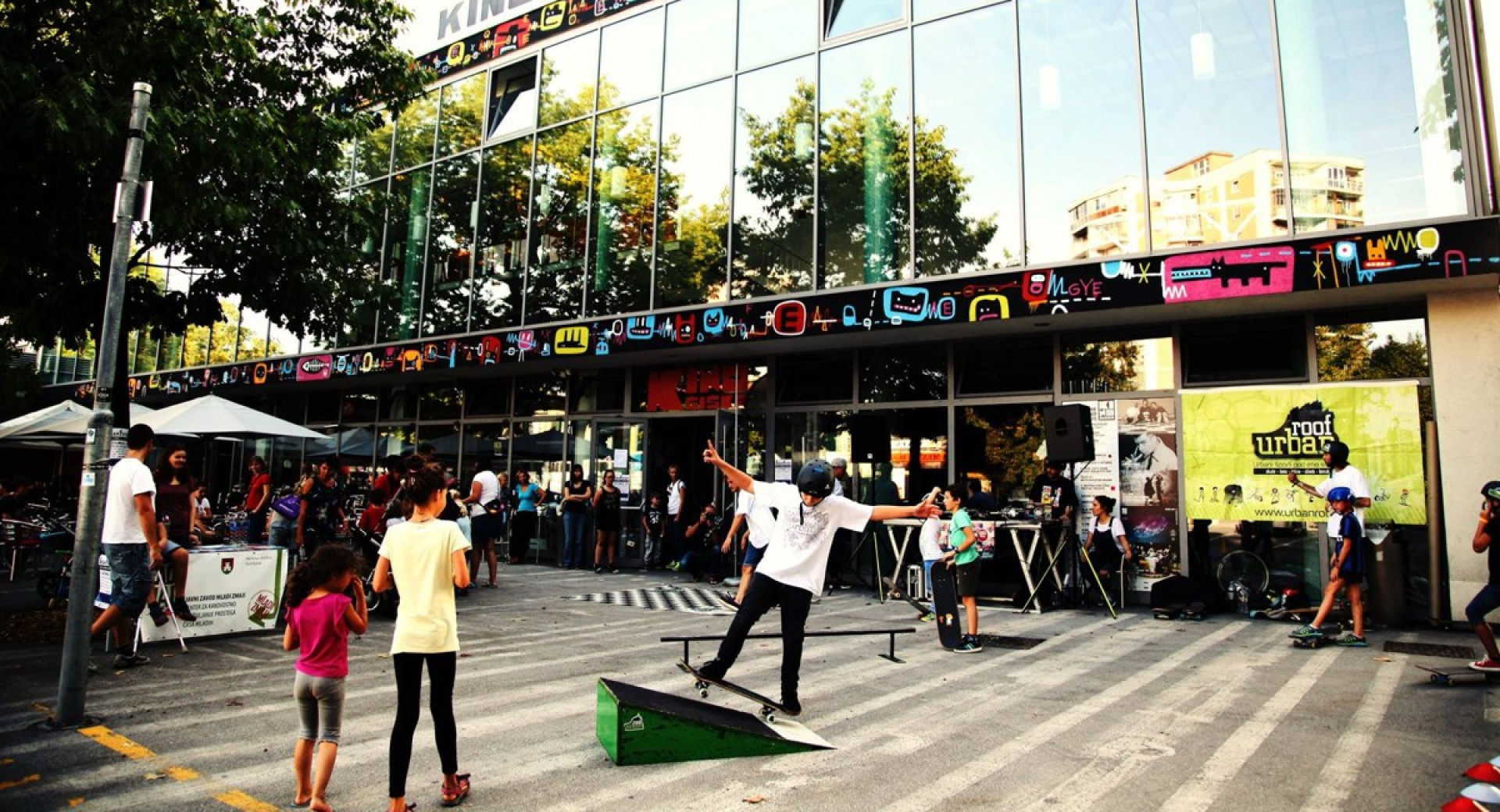 People in front of a large glass building. A boy is skateboarding in front of the building.