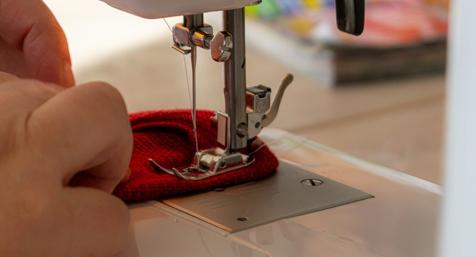 A sewing machine stitching red fabric, with one hand gently guiding the material under the needle.