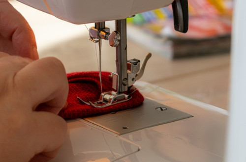 A sewing machine stitching red fabric, with one hand gently guiding the material under the needle.