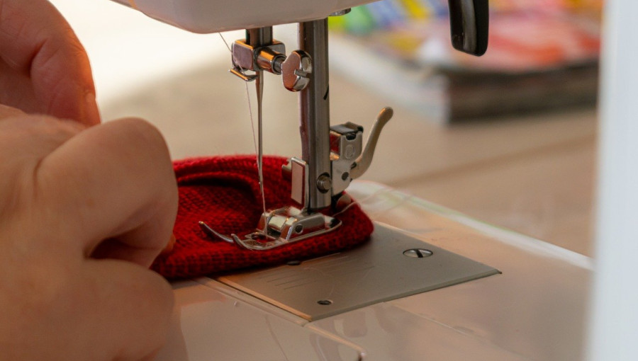 A sewing machine stitching red fabric, with one hand gently guiding the material under the needle.