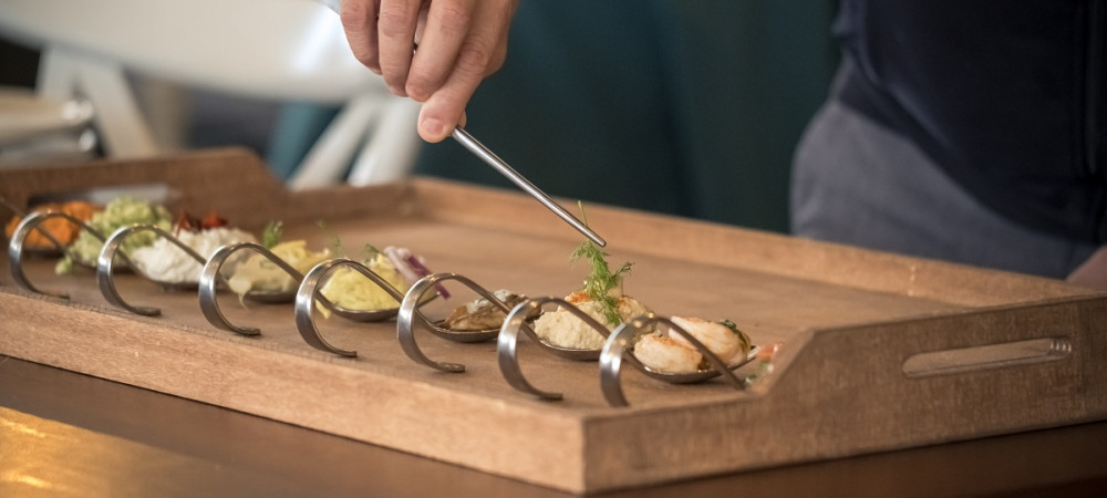 Silver spoons with portions of food. Chef with tweezers.