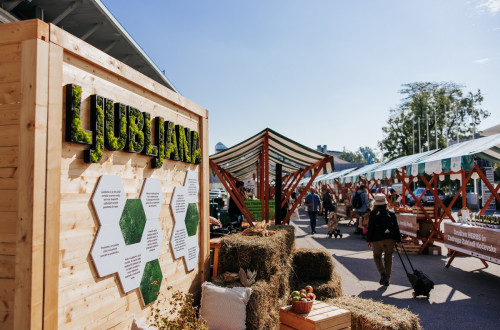 A market with stalls, featuring a prominent green sign that reads "Ljubljana."