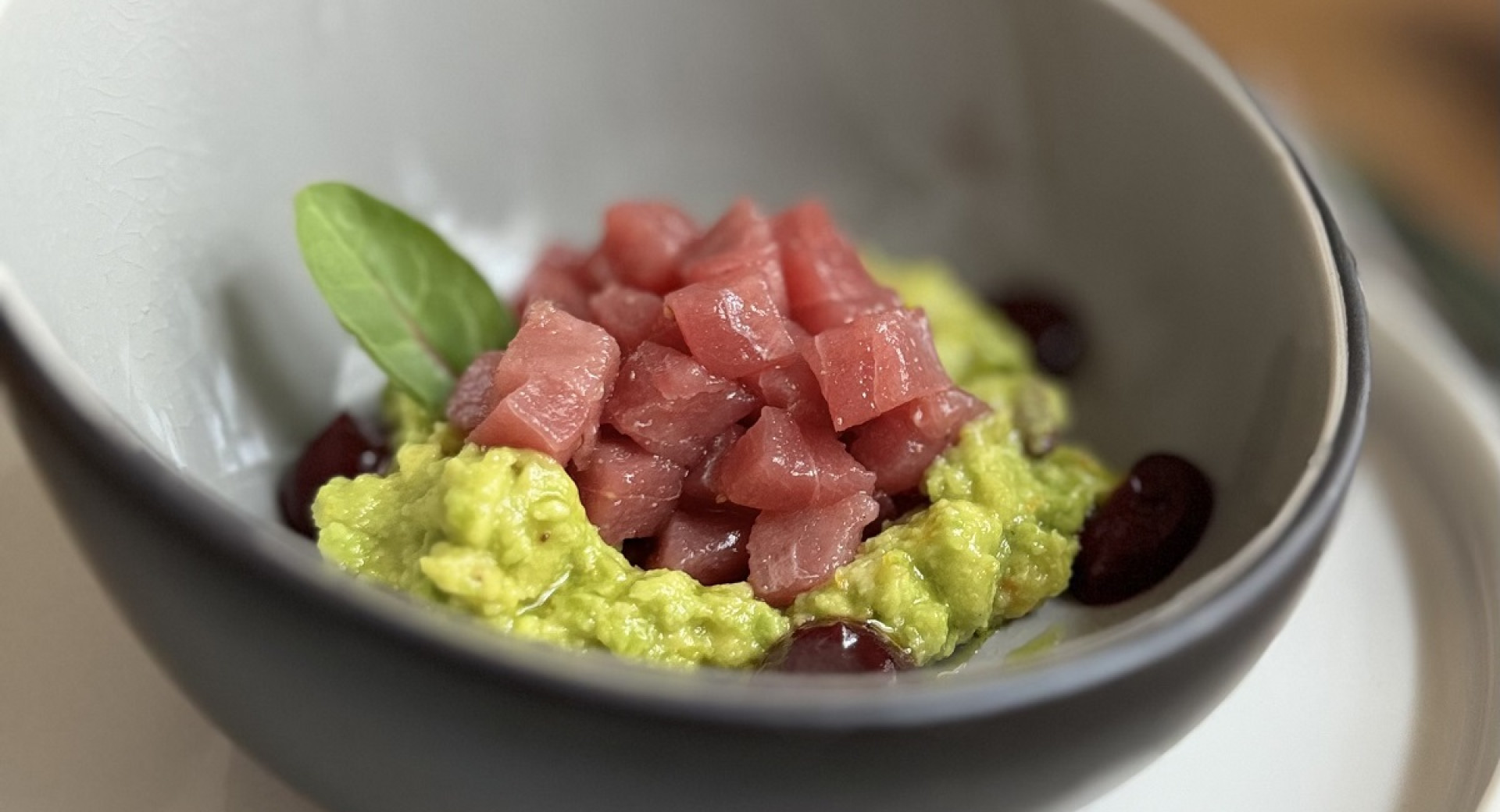 A gray bowl with green puree, topped with cubes of red meat.