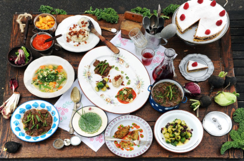 A large number of plates with food on a wooden table.