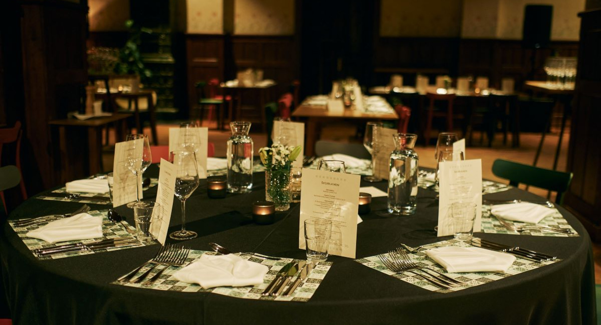 A round table is set with a black tablecloth and white menu cards.