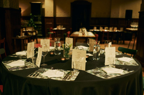 A round table is set with a black tablecloth and white menu cards.