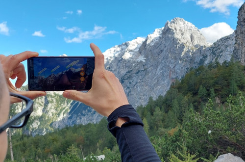 Moski drzi v rokah telefon in z njim fotografira pogled na gore.