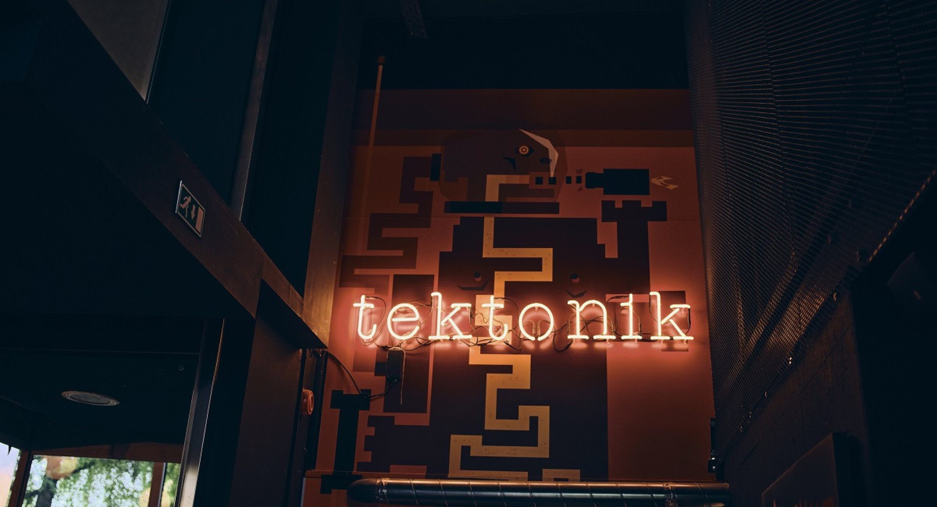 A lit sign reading "Tektonik" in the middle of a dark wall.