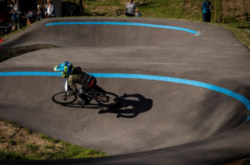 Pumptrack steza z modrimi crtami, po kateri se vozi otrok na kolesu z zascitno opremo.