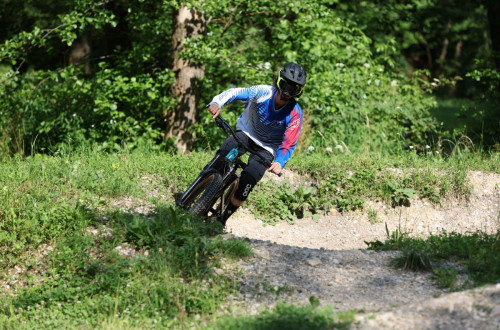 A cyclist on a forest path between turns, surrounded by greenery and trees.