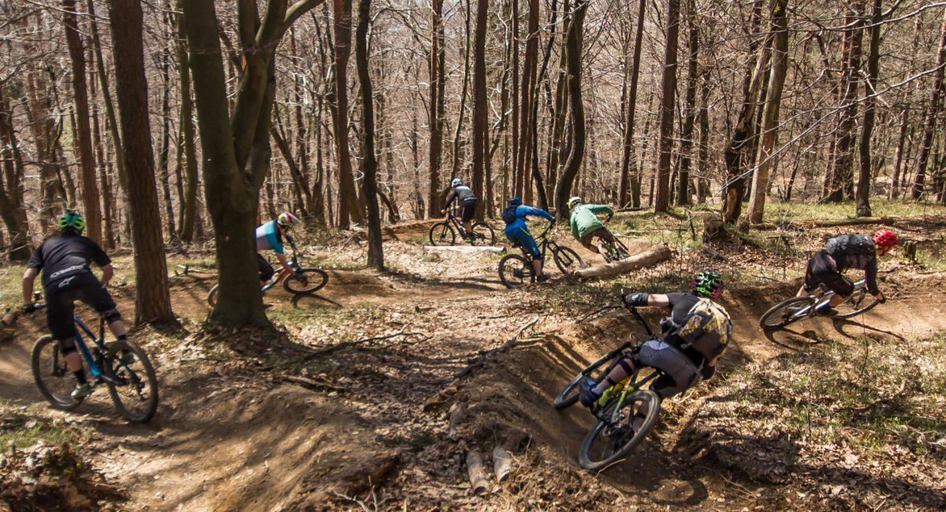 A group of mountain bikers on a winding forest path surrounded by trees.