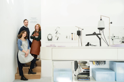 A modern jewelry studio with three artisans posing near a workspace equipped with tools and machinery.