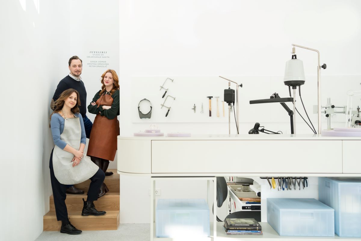 A modern jewelry studio with three artisans posing near a workspace equipped with tools and machinery.