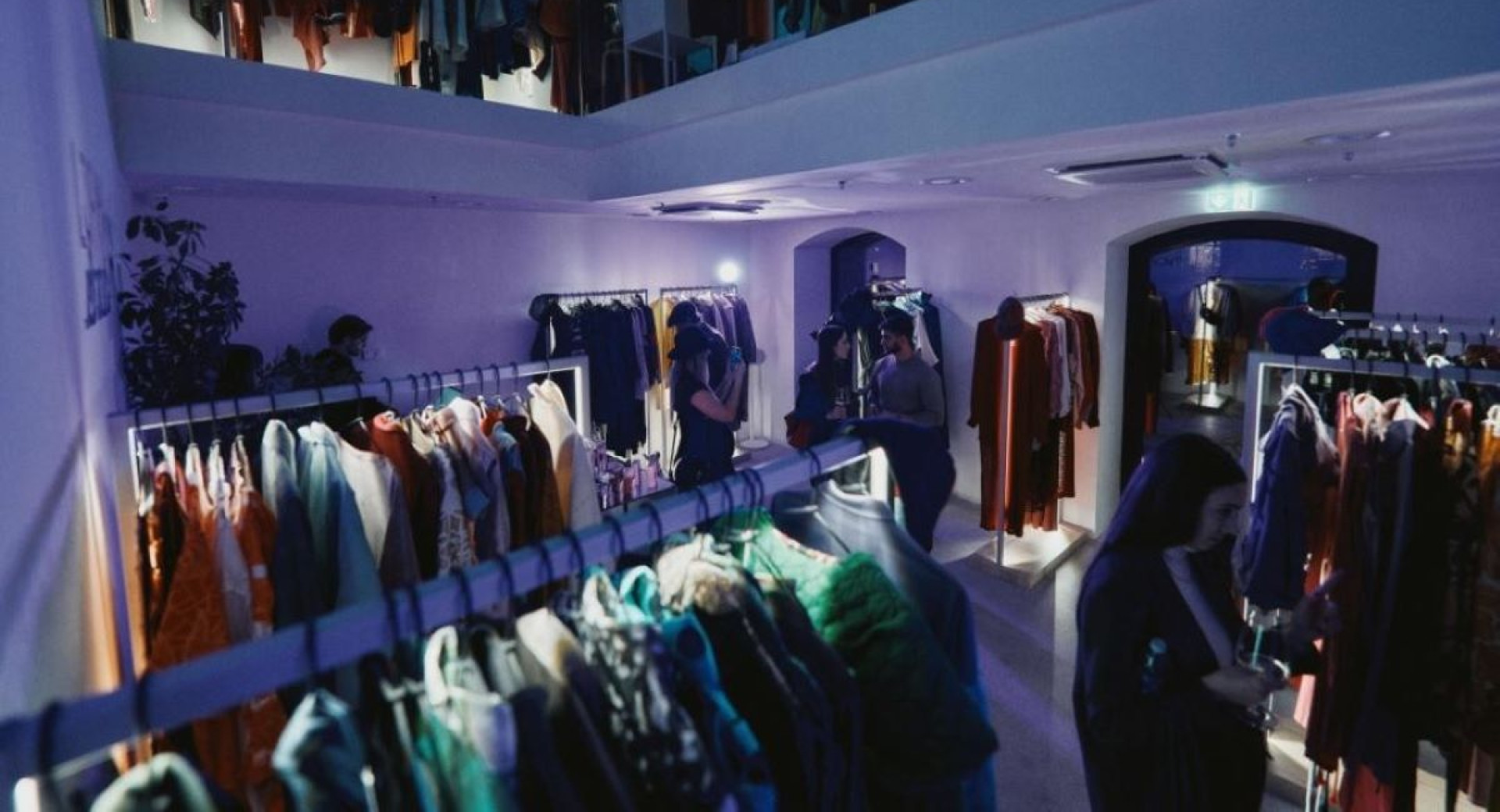 A bright space with a store where people are talking and browsing clothes displayed on hangers, illuminated.