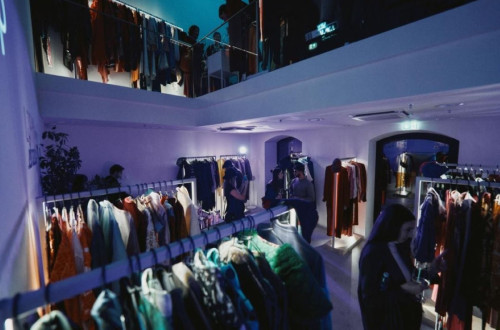 A bright space with a store where people are talking and browsing clothes displayed on hangers, illuminated.