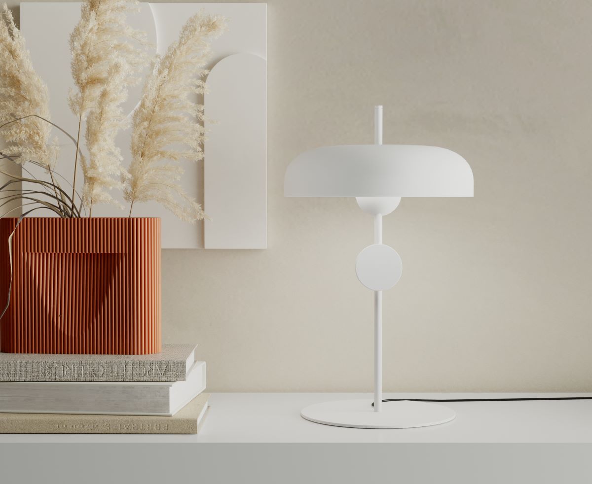 A modern minimalist interior with a white designer lamp, a textured terracotta vase with pampas grass, and a stack of books on a sleek white surface.