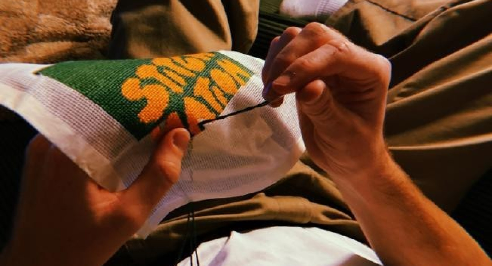 A person relaxing on a couch, carefully embroidering a colorful design on fabric.